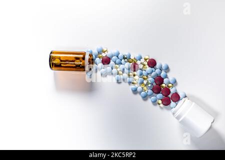 Eine Draufsicht auf mehrere bunte Pillen, die aus Glas- und Plastikflaschen auf weißem Hintergrund verschüttet werden Stockfoto
