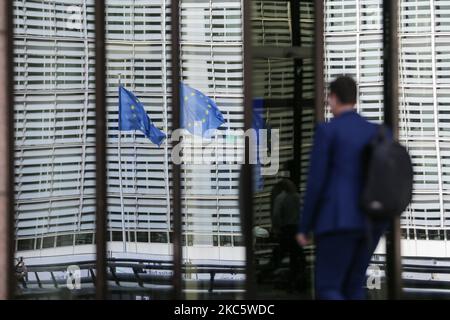 Spiegelung europäischer Flaggen, während ein Mann ein Gebäude betreten hat. Die Flaggen Europas winken, wie man sie an einem Mast sieht. Die Europäische Flagge ist das Symbol des COE des Europarates und der EU der Europäischen Union, wie sie in der belgischen Hauptstadt vor modernen Architekturgebäuden mit Glas- und Stahlkonstruktion, dem Gebäude Le Berlaymont, dem Sitz der Europäischen Kommission neben dem Forum Europa im Europäischen Viertel in Brüssel, zu sehen ist. Wo sich der Hauptsitz der gesamteuropäischen Institutionen und Organisationen befindet. Brüssel, Belgien am 2020. Oktober (Foto von Nicolas Economou/NurPhoto) Stockfoto