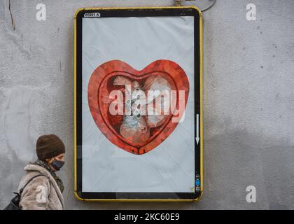 Eine Dame geht neben einer zerstörten Plakatwand mit einem Bild eines in einem herzförmigen Mutterleib von Ekaterina Glazkova, gesehen in Krakau (Foto aufgenommen am 9. Dezember 2020 in Krakau). Die 30-jährige unabhängige Künstlerin Ekaterina Glazkova aus St. Petersburg wurde dank der Stiftung „Unsere Kinder – Bildung, Gesundheit, Glaube“ aus Kornice in Schlesien unerwartet in Polen berühmt. Die Zeichnung einer russischen Frau - eines Kindes im Mutterleib -, die auf Plakaten und Plakaten in verschiedenen polnischen Städten auftaucht, ist zu einem Symbol der Anti-Abtreibungsbewegung geworden. Allerdings, wie laut Aussage des Künstlers auf Instagram o Stockfoto