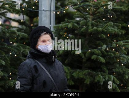 Eine Frau mit ihrer Gesichtsmaske geht in Kiew, Ukraine, am 21. Dezember 2020 an mit Lichtern geschmückten Weihnachtsbäumen vorbei. Die Zahl der bestätigten Covid-19-Fälle ist in der Ukraine die dritte Woche in Folge rückläufig (Foto: Sergii Kharchenko/NurPhoto) Stockfoto