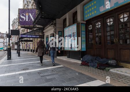 Ein Paar geht an einer Obdachlosen vorbei, die in einem geschlossenen Theater im West End Schutz sucht, da die Einschränkungen für das Coronavirus der Stufe 4 bestehen, um die Ausbreitung des neuen Coronavirus-Stamms zu begrenzen, während die Infektionen weiter zunehmen, am 22. Dezember 2020 in London, England. London, der Südosten und der Osten Englands traten am Sonntag in die Tier-4-Beschränkungen ein, ähnlich wie die letzte nationale Sperre, mit dem Befehl, zu Hause zu bleiben, dem Verbot der Vermischung von Haushalten, der Schließung aller nicht notwendigen Einzelhandels- und Geschäftsbetriebe und der Aufhebung der geplanten Lockerung der Regeln über fünf Tage um Weihnachten. (Pho Stockfoto