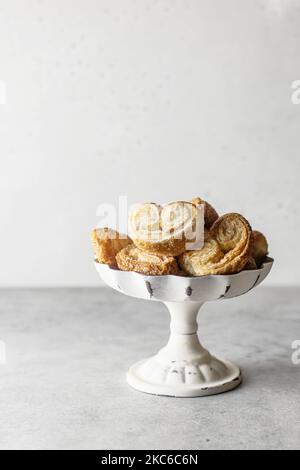 Blätterteig Plätzchen palmier oder Elefantenohren, knusprig Gebäck Herz in weißer Schale auf grauem Hintergrund isoliert geformt Stockfoto