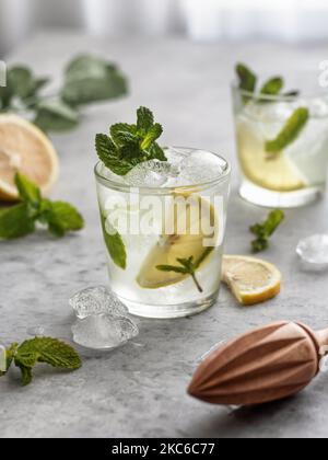 Frisch gebackene Limonade mit Zitrone und Minze in Glas auf grauem Hintergrund, mit entgiftetem Wasser angereichert Stockfoto