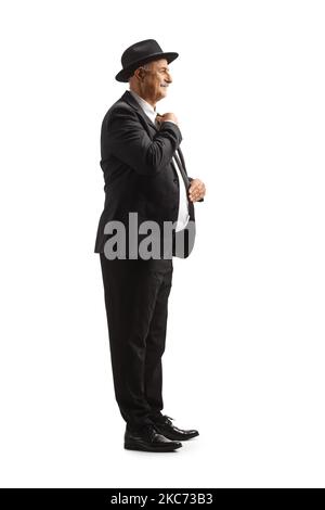 In voller Länge Profilaufnahme eines eleganten reifen Mannes, der sich fertig gemacht hat und seine Kleidung auf weißem Hintergrund isoliert sortiert Stockfoto