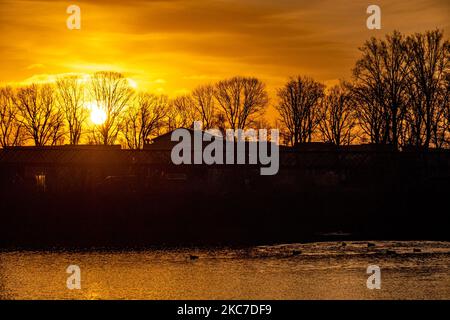 Sonnenaufgang Himmel ovre den See mit Reflexion auf dem Wasser. Frühmorgens tägliches Leben in den Niederlanden. Wintersonnenaufgang in der Region Nordbrabant mit der orangefarbenen hellen Sonne während der magischen Stunde, die einen bunten Himmel mit einigen Wolken und Silhouetten von Bäumen, Gebäuden, Menschen oder Vögeln vor sich bildet. Die Temperaturen unter dem Gefrierpunkt in der Nacht bilden während des eisigen Wetters etwas Frost. Meerhoven - Eindhoven am 13. Januar 2020 (Foto: Nicolas Economou/NurPhoto) Stockfoto