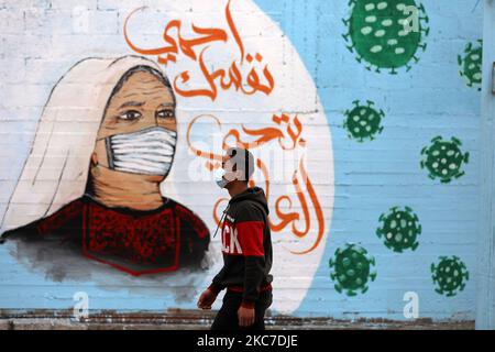 Ein palästinensischer Junge geht an Graffiti vorbei, mit einem arabischen Slogan, der lautet: „Schütze dich und deine Familie“, inmitten der Pandemie von Covid-19 in Gaza-Stadt am 13. Januar 2021. (Foto von Majdi Fathi/NurPhoto) Stockfoto