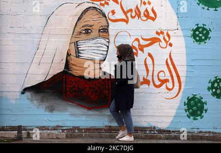 Eine Palästinenserin geht an Graffiti vorbei, mit einem arabischen Slogan, der lautet: „Schütze dich und deine Familie“, inmitten der Pandemie von Covid-19 in Gaza-Stadt am 13. Januar 2021. (Foto von Majdi Fathi/NurPhoto) Stockfoto