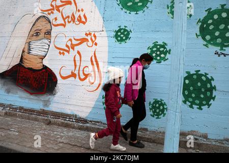 Palästinensische Kinder kommen an Graffiti vorbei, mit einem arabischen Slogan, der lautet: „Schütze dich und deine Familie“, inmitten der Pandemie von Covid-19 in Gaza-Stadt am 13. Januar 2021. (Foto von Majdi Fathi/NurPhoto) Stockfoto