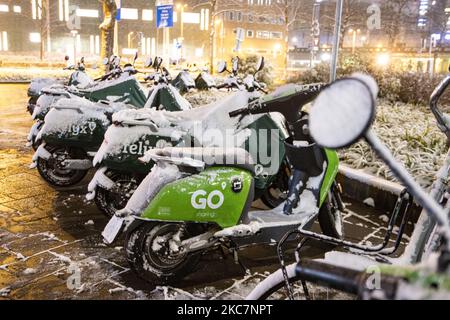 Schneebedeckte Elektroroller von GO-Sharing und Felyx Unternehmen. Tausende von schneebedeckten Fahrrädern, die in der Nähe des Bahnhofs geparkt sind. Nachtaufnahmen mit Langzeitbelichtung Bilder von schneebedeckten und beleuchteten Stadtlichtern Eindhoven Stadtzentrum nach dem Schneefall. Tägliches Leben in den Niederlanden mit dem ersten Schneefall des Jahres, der fast alles abdeckt, zeigt das kalte Wetter eine Temperatur unter Null. Der kälte Zustand mit Schnee und Eis änderte sich laut Prognose bald, der eisige Zustand wird nicht mehr als einen Tag dauern. Eindhoven, Niederlande am 16. Januar 2020 (Foto: Stockfoto