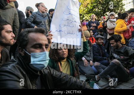 Junge Demonstranten sitzen auf dem Boden, heben ein Plakat auf, auf dem auf Arabisch steht: ‘Verarmung mich nicht, schweige mich nicht, unterdrücke mich nicht, marginalisiere mich nicht, Entweder Sie töten mich oder Sie lassen mich leben“, als sie an einer Anti-Regierungsdemonstration in der Avenue Habib Bourguiba in der Hauptstadt Tunis, Tunesien, am 19. Januar 2021 teilnahm, um gegen die Regierung des Premierministers Hichem Mechichi zu protestieren, Und zur Unterstützung der Protestbewegungen, die Tunesien in mehreren Städten über Nacht in den vergangenen Tagen getroffen haben. Demonstranten prallten mit den Sicherheitskräften zusammen, die Tränengas abfeuerten und Pfefferspray i verwendeten Stockfoto