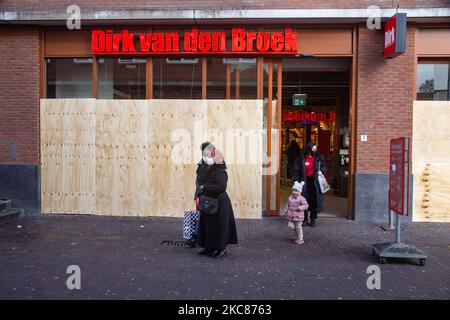 Nach den nächtlichen Unruhen beschädigte Dirk van den Broek Supermarkt mit den Fenstern, die mit Holzplatten vertäftet waren. Die Folgen der Unruhen in Rotterdam gegen die Ausgangssperre. Beschädigte Fenster von Geschäften, Cafés, Fast-Food-Kette, zerstörter Bürgersteig, kaputte Geldautomaten, Bushaltestellen, Straßenbahnhaltestellen, beschädigte Fenster und Gläser sogar in einem Wohngebiet wurden durch die gewalttätigen Demonstranten verursacht, die mit der Polizei zusammenprallten und das Gebiet um Groene Hilledijk, Beijerlandselaan und Randweg plünderten. Es ist die 3. aufeinander folgende Nacht von Unruhen und Zusammenstößen mit der Politik, nachdem die Regierung die Ausgangssperre verhängt hat, um die s zu bekämpfen Stockfoto