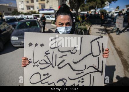 Eine junge Protesterin hält ein Plakat, auf dem auf Arabisch steht: ‘„Würde und Freiheit für beliebte Viertel“, während sie während eines protestmarsches, der im beliebten und harten Viertel Hay Ettadhamen, einer der bevölkerungsreichsten Städte Tunis, begann, für Bilder posiert. Und ging in Richtung Bardo City in Tunis, um gegen die Brutalität der Polizei, die Marginalisierung und die wirtschaftliche und soziale Krise im Land zu protestieren. Demonstranten hatten auch die Freilassung von Jugendlichen gefordert, die während der letzten nächtlichen Proteste, bei denen sie mit den Sicherheitskräften zusammenprallten, von der Polizei verhaftet wurden. Sicherheit Stockfoto