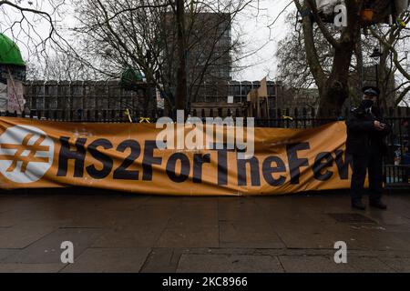 Ein Polizeibeamter steht neben einem Protestbanner, während die Polizei am 27. Januar 2021 in London, England, eine Operation zur Entfernung des Lagerplatzes eines ‘Stop HS2’-Lagers in den Euston Square Gardens ausführt. Trotz der Räumungen bleibt eine kleine Gruppe von Aktivisten in einem Tunnel, der heimlich unter dem Gelände errichtet wurde, um die nächste Phase der Arbeiten am Hochgeschwindigkeitsbahnprojekt zu verhindern, das London mit Birmingham, Manchester und Leeds verbinden soll. (Foto von Wiktor Szymanowicz/NurPhoto) Stockfoto