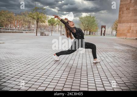 Blonde junge Frau in schwarzem Kleid, die im Regen auf der Straße tanzt. Tanzkonzept Stockfoto