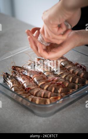 Ein vertikaler Schuss Hände, der köstliche Garnelen würzt Stockfoto