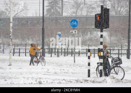 Menschen, die ihre Fahrräder tragen, weil es schwierig ist, auf dem Schnee zu fahren. Blizzard vom Schneesturm Darcy in den Niederlanden, dem ersten starken Schneefall mit starken Winden nach 2010, der den Transport im ganzen Land störte. Die Niederländer erwachten am Sonntag mit einer Schneeschicht, die alles bedeckte. Viele Unfälle ereigneten sich auf den Straßen aufgrund des Sturms und der eisigen Bedingungen, während es auch Probleme mit den Zügen gab. In der Stadt Eindhoven in Nordbrabant wurde der Bahn- und Busverkehr eingestellt, der Flughafen folgte und der Luftverkehr umgeleitet. Die Leute gingen nach draußen hinein Stockfoto
