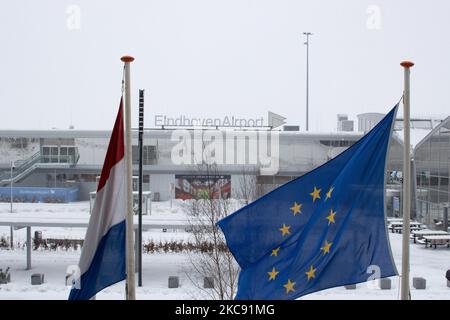 Logo des Flughafens Eindhoven mit europäischer und niederländischer Flagge. Schneesturm schließt den Flughafen Eindhoven EIN in den Niederlanden. Starker Schneefall stört den Flugverkehr, der am Sonntag zu Umleitungen nach Deutschland führte. Blizzard vom Sturm Darcy traf das Land seit Sonntagmorgen (07.02.2021), was zu Problemen bei den öffentlichen Verkehrsmitteln führte. Auf dem schneebedeckten Flughafen Eindhoven werden Transavia-Flugzeuge am Boden gesehen, während schwere Maschinen die Rollbahn und die Landebahn reinigen. Dutzende von Flügen, die abfliegen sollten, wurden am Flughafen Schiphol in Amsterdam aufgrund des arktischen kalten Winters, den wir hatten, verspätet oder gestrichen Stockfoto