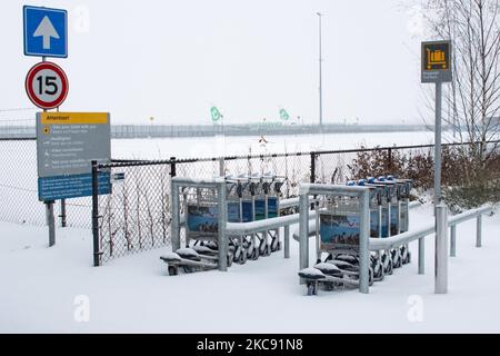 Gepäckwagen und geerdete Transavia-Flotte, Boeing 737 am Flughafen Eindhoven aufgrund des Schnees. Schneesturm schließt den Flughafen Eindhoven EIN in den Niederlanden. Starker Schneefall stört den Flugverkehr, der am Sonntag zu Umleitungen nach Deutschland führte. Blizzard vom Sturm Darcy traf das Land seit Sonntagmorgen (07.02.2021), was zu Problemen bei den öffentlichen Verkehrsmitteln führte. Auf dem schneebedeckten Flughafen Eindhoven werden Transavia-Flugzeuge am Boden gesehen, während schwere Maschinen die Rollbahn und die Landebahn reinigen. Dutzende von Flügen, die abfliegen sollten, wurden am Flughafen Schiphol in Einem Verspätet oder gestrichen Stockfoto