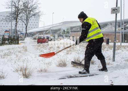 Ein Mann mit gelber Weste schaufelt und reinigt den Weg um den Flughafen Eindhoven. Schneesturm schließt den Flughafen Eindhoven EIN in den Niederlanden. Starker Schneefall stört den Flugverkehr, der am Sonntag zu Umleitungen nach Deutschland führte. Blizzard vom Sturm Darcy traf das Land seit Sonntagmorgen (07.02.2021), was zu Problemen bei den öffentlichen Verkehrsmitteln führte. Auf dem schneebedeckten Flughafen Eindhoven werden Transavia-Flugzeuge am Boden gesehen, während schwere Maschinen die Rollbahn und die Landebahn reinigen. Dutzende von Flügen, die abfliegen sollten, wurden am Flughafen Schiphol in Amst verspätet oder gestrichen Stockfoto