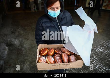 Eine Frau, die wegen der Ausbreitung des Coronavirus eine Gesichtsmaske trägt, hält eine Schachtel Donuts, die sie für Fat Thursday gekauft hat. Krakau, Polen, am 11. Februar 2021. Fat Thursday ist ein traditionelles katholisches christliches Fest am letzten Donnerstag vor der Fastenzeit. Es symbolisiert die Feier des Karnevals. Das beliebteste Gericht, das an diesem Tag in Polen serviert wird, sind Paczki - faustgroße Donuts, gefüllt mit Marmelade. (Foto von Beata Zawrzel/NurPhoto) Stockfoto