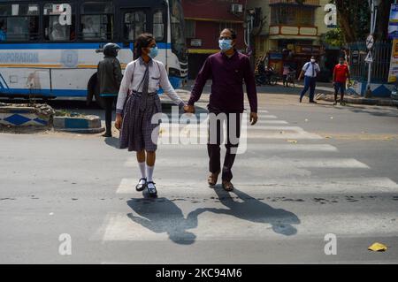 Ein Vater hilft ihrer Tochter am 12. Februar 2021, die Straße vor einer Schule in Kalkutta, Indien, zu überqueren. Die Regierung Westbengals gab am Freitag die Erlaubnis, die gesamte Regierung und Privatschule von der Klasse 9 bis 12 wieder zu öffnen, nachdem sie wegen COVID-19 für mehr als 11 Monate geschlossen worden war. Schüler und Lehrer werden angewiesen, während des Unterrichts die strengen COVID-19-Protokolle zu befolgen. (Foto von Debarchan Chatterjee/NurPhoto) Stockfoto