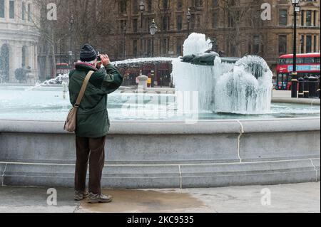 Ein Mann macht am 12. Februar 2021 in London, England, ein Foto einer gefrorenen Meerjungfrau-Statue im Brunnen am Trafalgar Square an einem kalten Wintertag, an dem England unter der dritten Sperre bleibt, um die Covid-19-Infektionsraten zu reduzieren. (Foto von Wiktor Szymanowicz/NurPhoto) Stockfoto