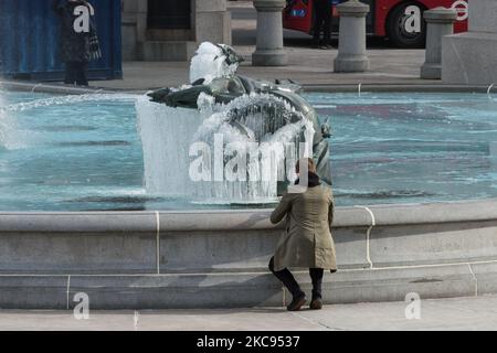 Ein Mann macht am 12. Februar 2021 in London, England, ein Foto einer gefrorenen Meerjungfrau-Statue im Brunnen am Trafalgar Square an einem kalten Wintertag, an dem England unter der dritten Sperre bleibt, um die Covid-19-Infektionsraten zu reduzieren. (Foto von Wiktor Szymanowicz/NurPhoto) Stockfoto