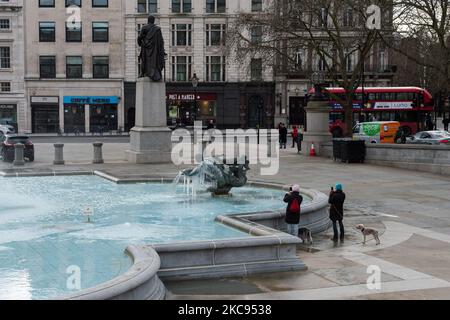 An einem kalten Wintertag, an dem England noch unter der dritten Sperre steht, um die Covid-19-Infektionsrate zu senken, fotografieren Menschen am 12. Februar 2021 in London, England, eine gefrorene Statue der Meerjungfrau im Brunnen am Trafalgar Square. (Foto von Wiktor Szymanowicz/NurPhoto) Stockfoto