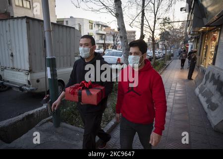 Ein iranischer Mann mit einer schützenden Gesichtsmaske, die ein Geschenk zum Valentinstag trägt, während er mit seinem Freund inmitten des COVID-19-Ausbruchs im Iran am 12. Februar 2021 entlang einer Straße in der Innenstadt von Teheran spaziert. (Foto von Morteza Nikoubazl/NurPhoto) Stockfoto