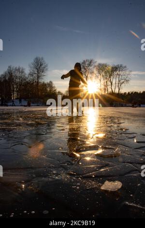 Dunkle Silhouetten von Menschen beim Eislaufen auf dem kristallklaren natürlichen gefrorenen See in der Region Nordbrabant am Nachmittag vor dem Sonnenuntergang. Eislaufrausch übernimmt die Niederlande. Die Niederländer haben viel Spaß und genießen das einwöchige, kalte Schneewetter mit Temperaturen unter Null, die dazu führen, dass Seen, Bäche, Teiche, Flüsse und Kanäle gefrieren. Im Park Meerland in der Nähe der Stadt Eindhoven haben sich die Massen an einem sonnigen Tag mit blauem Himmel abgesetzt, da es eine niederländische Tradition ist. Außerdem werden die Menschen im Freien in der eisgefrorenen Natur und der kalten Umgebung gesehen, die auf dem Eis der gefrorenen Seen spazieren gehen, p Stockfoto