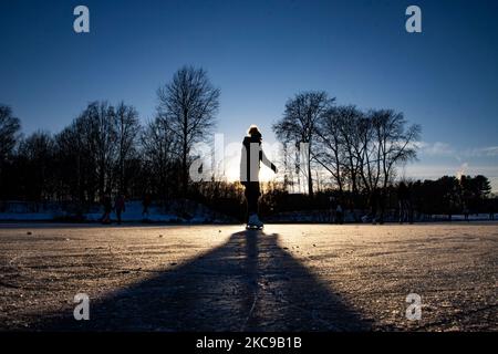 Dunkle Silhouetten von Menschen beim Eislaufen auf dem kristallklaren natürlichen gefrorenen See in der Region Nordbrabant am Nachmittag vor dem Sonnenuntergang. Eislaufrausch übernimmt die Niederlande. Die Niederländer haben viel Spaß und genießen das einwöchige, kalte Schneewetter mit Temperaturen unter Null, die dazu führen, dass Seen, Bäche, Teiche, Flüsse und Kanäle gefrieren. Im Park Meerland in der Nähe der Stadt Eindhoven haben sich die Massen an einem sonnigen Tag mit blauem Himmel abgesetzt, da es eine niederländische Tradition ist. Außerdem werden die Menschen im Freien in der eisgefrorenen Natur und der kalten Umgebung gesehen, die auf dem Eis der gefrorenen Seen spazieren gehen, p Stockfoto
