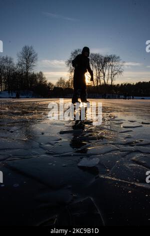 Dunkle Silhouetten von Menschen beim Eislaufen auf dem kristallklaren natürlichen gefrorenen See in der Region Nordbrabant am Nachmittag vor dem Sonnenuntergang. Eislaufrausch übernimmt die Niederlande. Die Niederländer haben viel Spaß und genießen das einwöchige, kalte Schneewetter mit Temperaturen unter Null, die dazu führen, dass Seen, Bäche, Teiche, Flüsse und Kanäle gefrieren. Im Park Meerland in der Nähe der Stadt Eindhoven haben sich die Massen an einem sonnigen Tag mit blauem Himmel abgesetzt, da es eine niederländische Tradition ist. Außerdem werden die Menschen im Freien in der eisgefrorenen Natur und der kalten Umgebung gesehen, die auf dem Eis der gefrorenen Seen spazieren gehen, p Stockfoto
