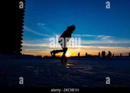 Dunkle Silhouetten von Menschen beim Eislaufen auf dem kristallklaren natürlichen gefrorenen See in der Region Nordbrabant am Nachmittag vor dem Sonnenuntergang. Eislaufrausch übernimmt die Niederlande. Die Niederländer haben viel Spaß und genießen das einwöchige, kalte Schneewetter mit Temperaturen unter Null, die dazu führen, dass Seen, Bäche, Teiche, Flüsse und Kanäle gefrieren. Im Park Meerland in der Nähe der Stadt Eindhoven haben sich die Massen an einem sonnigen Tag mit blauem Himmel abgesetzt, da es eine niederländische Tradition ist. Außerdem werden die Menschen im Freien in der eisgefrorenen Natur und der kalten Umgebung gesehen, die auf dem Eis der gefrorenen Seen spazieren gehen, p Stockfoto