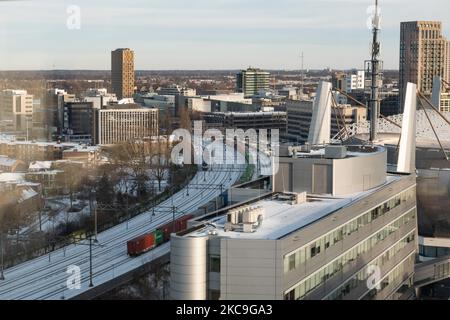 Eine Ladung und ein Personenzug auf den schneebedeckten Schienen im Stadtzentrum. Panorama-Übersicht über die schneebedeckte niederländische Stadt Eindhoven, wie sie im Zentrum und in den Wohngebieten zu sehen ist, während der Schnee über einen Zeitraum von mehr als einer Woche die Straßen, die Eisenbahn und die Dächer bedeckte, wodurch auch Seen und Kanäle gefrieren konnten. Eindhoven, Niederlande am 2021. Februar (Foto: Nicolas Economou/NurPhoto) Stockfoto