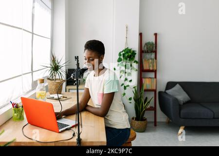 Lächelnde junge afrikanische Frau, die Podcast im modernen Studio zu Hause aufzeichnet Stockfoto