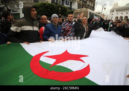 Algerier halten eine Nationalflagge mit der arabischen Inschrift, die die Erwähnung trägt, während sie zum zweiten Jahrestag der Volksproteste in Algier, Algerien, am 22. Februar 2021 marschieren. Algerien feiert den zweiten Jahrestag der Bewegung am 22. Februar 2021 Massenprotest, bekannt als Hirak, der zum Rücktritt des damaligen Präsidenten Abdelaziz Bouteflika führte. Der amtierende algerische Präsident Abdelmadjid Tebbounne kündigte am 18. Februar die Begnadigung und Freilassung von etwa sechzig Personen an, die aufgrund ihrer Beteiligung an der Hirak-Protestbewegung verurteilt oder auf ein Gerichtsverfahren warten. Er sagte auch, dass er es war Stockfoto