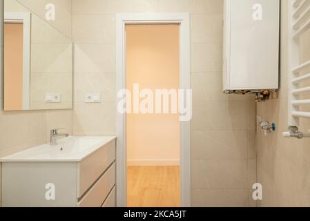 Badezimmer mit kleiner, weißer Kommode mit Schubladen und rahmenlosem rechteckigem Spiegel über dem Resin-Waschbecken Stockfoto