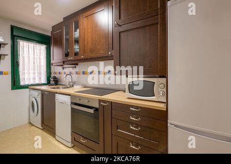 Küche mit dunklen Holzmöbeln und integrierten Geräten in verschiedenen Farben Stockfoto