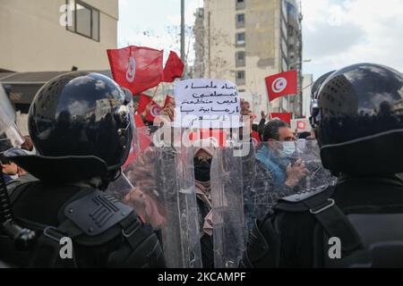 Eine Protesterin islamistischer Bewegungen steht vor den Sicherheitskräften, als sie ein Plakat mit der Aufschrift „die Internationale Union für muslimische Gelehrte ist keine terroristische Gruppe“ auf Arabisch aufhebt. Während einer Demonstration, die am 10. März 2021 vor dem Hauptquartier der tunesischen Zweigstelle der Internationalen Union für muslimische Gelehrte (IUMS) in der tunesischen Hauptstadt Tunis stattfand, um gegen den Präsidenten der Freien Destourien Partei (PDL), Abir Moussi und ihre Anhänger zu protestieren, Die einen Sit-in vor dem Hauptquartier der IUL halten, um ihre Auflösung zu fordern. (Foto von Chedly Ben Ibrahim/NurPhot Stockfoto