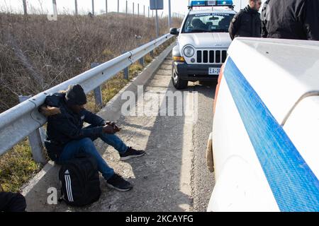 Auf der Autobahn in der Nähe der Stadt Orestiada in der Region Evros, Thrakien, in Griechenland, befinden sich Polizeiautos und Polizeibeamte, die 2 Migranten ohne Papiere halten, einen aus Afghanistan und einen aus Afrika, die illegal die Grenzen der Türkei überquerten. Der Evros-Fluss oder Martisa oder Meric ist die südöstlichere Außengrenze der EU und des Schengen-Raums. Asylbewerber werden entlang der griechisch-türkischen Grenzen gefangen genommen, während sie versuchen, nach Griechenland und in die Europäische Union einzureisen. Die hellenische Polizei und Frontex-Truppen machen die Grenzpatrouille und nehmen täglich fest oder verhaften Migranten, Flüchtlinge und Schmuggler auf den griechischen Stockfoto