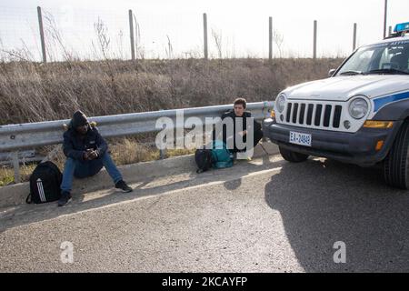 Auf der Autobahn in der Nähe der Stadt Orestiada in der Region Evros, Thrakien, in Griechenland, befinden sich Polizeiautos und Polizeibeamte, die 2 Migranten ohne Papiere halten, einen aus Afghanistan und einen aus Afrika, die illegal die Grenzen der Türkei überquerten. Der Evros-Fluss oder Martisa oder Meric ist die südöstlichere Außengrenze der EU und des Schengen-Raums. Asylbewerber werden entlang der griechisch-türkischen Grenzen gefangen genommen, während sie versuchen, nach Griechenland und in die Europäische Union einzureisen. Die hellenische Polizei und Frontex-Truppen machen die Grenzpatrouille und nehmen täglich fest oder verhaften Migranten, Flüchtlinge und Schmuggler auf den griechischen Stockfoto