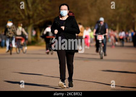 Eine Frau mit Gesichtsmaske joggt am 29. März 2021 in der warmen Frühlingssonne am Serpentine Lake im Hyde Park in London, England. Heute wurden in ganz England Lockdown-Beschränkungen gelockert, mit dem Ende der Regel „Heimtagebaucht“, Gruppen von bis zu sechs Personen durften sich draußen treffen, Outdoor-Sportarten wurden wieder aufgenommen und Hochzeiten mit bis zu sechs Teilnehmern durften Schieß los. besuchen. Geschäfte, Gastgewerbe- und Freizeitbetriebe bleiben jedoch geschlossen, wobei die nächste Lockerung der Beschränkungen frühestens im April 12 fällig ist. Die heutige Lockerung fiel inzwischen mit der ersten einer dreitägigen „Mini-Hitzewelle“ zusammen, mit d Stockfoto