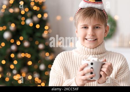 Kleiner Junge, der am Heiligabend zu Hause eine Tasse Kakao mit Sümpfen hält Stockfoto