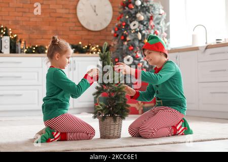 Kleine Kinder, die in der Küche als Elfen gekleidet waren, die den Weihnachtsbaum dekorierten Stockfoto