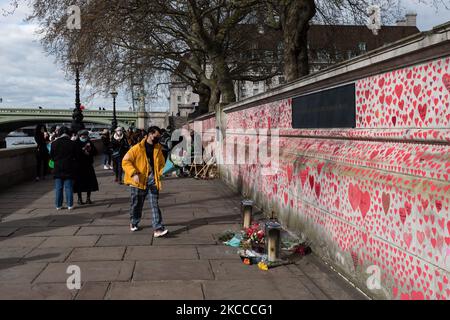 LONDON, GROSSBRITANNIEN - 07. APRIL 2021: Ein Mitglied der Öffentlichkeit legt am 07. April 2021 in London, England, Blumen an ein Denkmal für die Opfer von Covid-19 vor dem St. Thomas’ Hospital. Das Wandbild, das Covid-19 Hinterbliebene Familien für Gerechtigkeit am Montag vergangener Woche eingerichtet hat, hat bisher rund 130.000 handgezeichnete Herzen auf einem kilometerlangen Mauerabschnitt vor dem Parlament gesehen. (Foto von Wiktor Szymanowicz/NurPhoto) Stockfoto