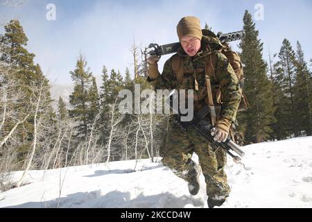 Die US Marine trägt den Empfänger eines Maschinengewehrs des Kalibers .50, während er durch den Schnee stapft. Stockfoto