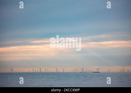 Offshore-Windpark mit Windmühlen, die grüne erneuerbare elektrische Energie erzeugen, 20 Kilometer von der niederländischen Küste entfernt, zwischen den Niederlanden und dem Vereinigten Königreich, während der Abenddämmerung, mit Wolken und Schiffen über dem Horizont des Meeres. Die Windkraftanlagen erzeugen nachhaltige grüne Energie aus der Windkraft, den Luftstrom in der Atmosphäre, den in der Nordsee installierten Park aus der Sicht von Oosterschelde in Zeeland, Niederlande, am 10. April 2021 (Foto: Nicolas Economou/NurPhoto) Stockfoto
