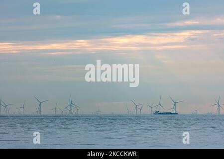 Offshore-Windpark mit Windmühlen, die grüne erneuerbare elektrische Energie erzeugen, 20 Kilometer von der niederländischen Küste entfernt, zwischen den Niederlanden und dem Vereinigten Königreich, während der Abenddämmerung, mit Wolken und Schiffen über dem Horizont des Meeres. Die Windkraftanlagen erzeugen nachhaltige grüne Energie aus der Windkraft, den Luftstrom in der Atmosphäre, den in der Nordsee installierten Park aus der Sicht von Oosterschelde in Zeeland, Niederlande, am 10. April 2021 (Foto: Nicolas Economou/NurPhoto) Stockfoto