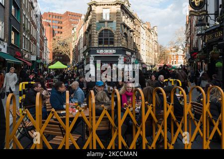 LONDON, GROSSBRITANNIEN - 12. APRIL 2021: Menschenmassen füllen Tische in der Old Compton Street in Soho, die für den Verkehr gesperrt ist, da die Gaststätten im Freien ihre Räumlichkeiten für Kunden öffnen, nachdem sie am 12. April 2021 in London, England, für mehr als drei Monate nach der Sperrung durch das Coronavirus geschlossen wurden. Ab heute geht die nächste Stufe der Aufhebung von Sperrbeschränkungen voran, indem Pubs und Restaurants erlaubt sind, Speisen und Getränke im Freien zu servieren, und die Eröffnung von nicht notwendigen Geschäften, Friseuren, Schönheitssalons und Fitnessstudios in England. (Foto von Wiktor Szymanowicz/NurPhoto) Stockfoto