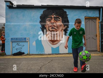 Johnny Figo Murphy, 9 Jahre alt, zeigt seine Fußballschuhe vor einem neuen Wandgemälde von CHELS (Chelsea Jacobs, ein in Dublin lebender amerikanischer Künstler), der Diego Maradona, einen der größten Spieler in der Geschichte des Fußballs, vertritt. Am Dienstag, den 13. April 2021, in Dublin, Irland. (Foto von Artur Widak/NurPhoto) Stockfoto